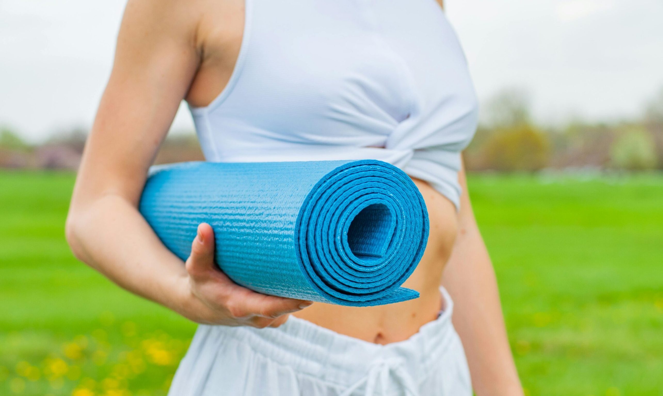 pexels photo 2394051 2394051 Close-up of a woman holding a blue yoga mat in a green outdoor setting during spring.
